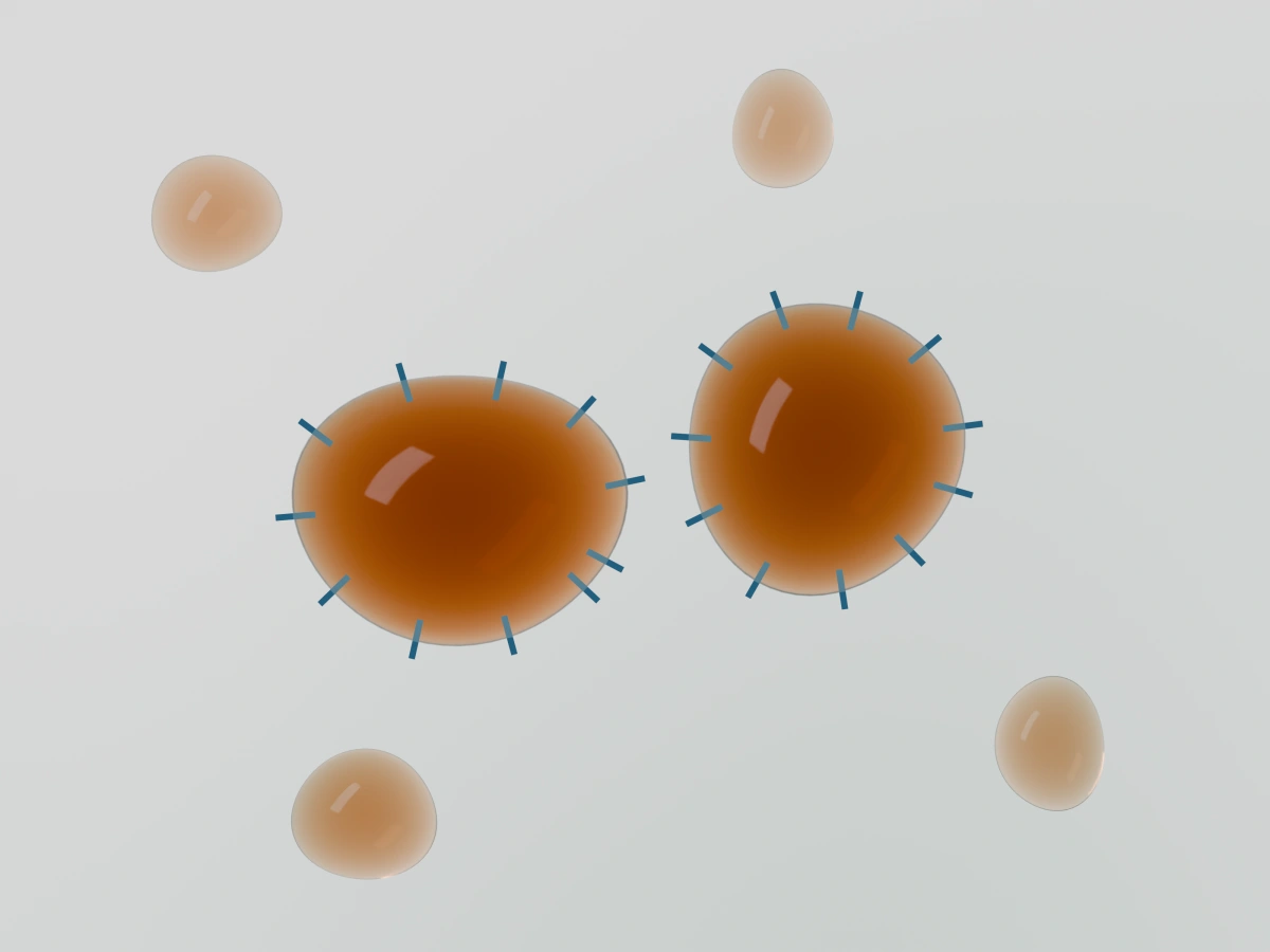 Enlarged schematic of amber tramp oil droplets in coolant, with blue markings representing emulsifiers at the droplet surfaces. The droplets remain separate rather than merging.